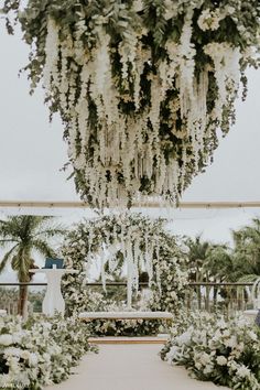 an outdoor wedding ceremony with white flowers and greenery hanging from the ceiling over the aisle