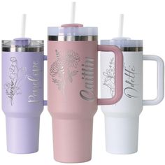 three different colored travel mugs with flowers on the side and one has a straw in it