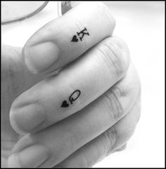 two fingers with small tattoos on them, one has an arrow and the other has a heart