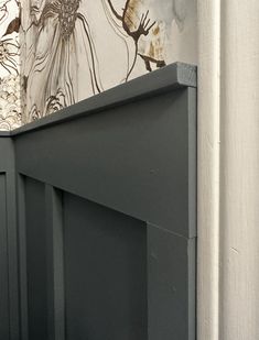 a cat sitting on top of a wooden cabinet next to a wall with flowers painted on it