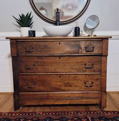 a wooden dresser with a bowl on top and a mirror above it, in front of a white wall