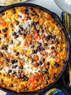 a skillet filled with black beans, cheese and tortilla chips on a table