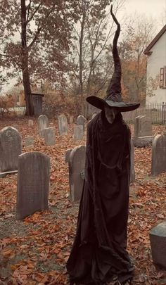 a person dressed up as a witch standing in the middle of a cemetery with leaves on the ground