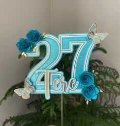 there is a blue cake with flowers on it and the number twenty seven behind it