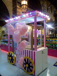 a pink and white popcorn cart with balloons on it's side in a store