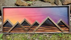 a wooden sign with mountains painted on it in front of some rocks and green grass