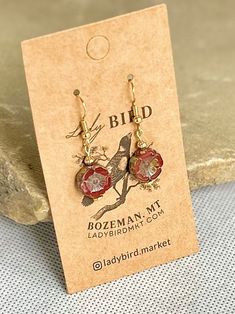 Czech glass coins in a shiny, vibrant burgundy red and etched in a wild rose shape. These nature-inspired glass dangle earrings are perfect for dressing up or down, adding a boho shimmer to vintage-inspired styles. Welcome to our Bohemian-inspired earring collection, where free-spirited fashion meets timeless elegance. Each pair of earrings is meticulously crafted with exquisite Czech glass floral beads, offering a touch of bohemian charm to any ensemble.Embrace individuality with our diverse ra Red Czech Glass Jewelry, Czech Glass Earrings As A Gift, Vintage Czech Glass Flower Earrings Gift, Vintage Czech Glass Flower Earrings For Gift, Red Round Jewelry With Flower Charm, Vintage Red Flower Earrings For Gift, Red Pressed Flowers Earrings For Gift, Red Pressed Flowers Round Jewelry, Red Round Jewelry With Pressed Flowers