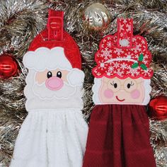 two oven mitts with santa claus and snowflakes on them, hanging from a christmas tree