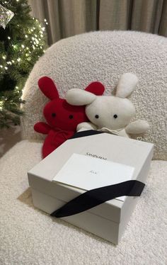 two stuffed animals sitting next to each other on a white chair near a christmas tree