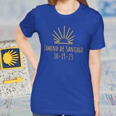 Cute Camino de Santiago keepsake souvenir tshirt gifts for completion of the Camino de Santiago de Compostela in Spain! The shirt is customized with the exact date the Camino was completed, making it a truly unique gift and personal memento.  A perfect t-shirt for a hike or a spiritual pilgrimage completed on the el Camino walk to Santiago de Compostela. This top is offered in six colors, including the color royal blue with yellow graphics--which are the symbolic colors of the Camino.  BTW - We have many Camino t-shirts, gifts & souvenirs: https://www.etsy.com/shop/GiftsByAuroraDesign?ref=seller-platform-mcnav&section_id=42884887 Thank you for choosing Gifts by Aurora Design. We have a passion for travel and fun adventures.  Check out our shop to see new items as they are introduced https: Blue Screen Print T-shirt As Gift, Blue Short Sleeve T-shirt For Gift, Summer T-shirt With Name Print For Gifts, Blue T-shirt With Name Print For Gift, Blue T-shirt With Name Print As Gift, Camino De Santiago Tattoo Ideas, Camino De Santiago Portuguese Coastal, Camino De Santiago Quotes Inspiration, Aurora Design