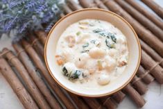 a white bowl filled with soup next to some sticks and lavender flowers on a table