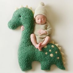 a baby sleeping on top of a green stuffed dinosaur