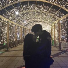 a man and woman standing under a canopy covered in christmas lights at night with their faces close to each other