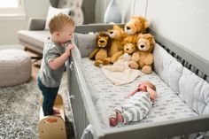 a little boy standing next to a baby in a crib