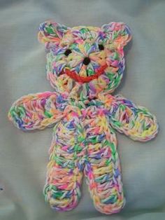 a multicolored crocheted teddy bear sitting on top of a white sheet