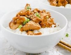 two white bowls filled with rice covered in chicken and sauce on top of chopsticks