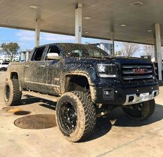 a black truck parked in front of a gas station with mud all over it's tires