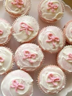 many cupcakes with pink bows on them are sitting on a white platter