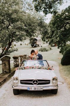 a bride and groom kissing in the back of a mercedes benz convertible parked on a driveway