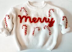 a white sweater with candy canes and the word merry written on it in red thread