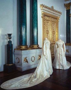 two wedding gowns are on display in a room with gold columns and green vases