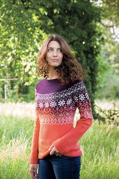 a woman standing in the grass with her hands on her hips, wearing a colorful sweater