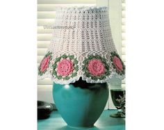 a crocheted lamp shade with pink flowers on it sitting on a blue table