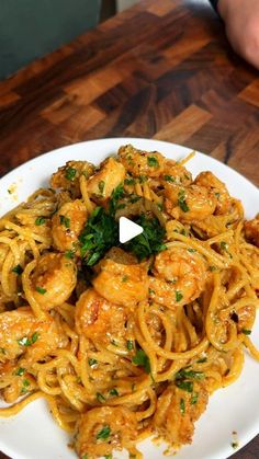 a white plate topped with pasta covered in sauce and shrimp next to a wooden table