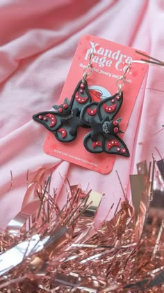 a pair of black cat earrings sitting on top of a pink sheet