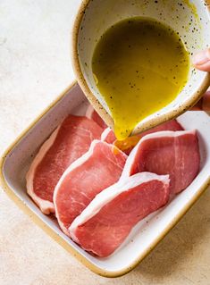 raw meat being poured into a bowl with olive oil in it on a counter top