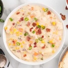 a white bowl filled with soup next to two bowls of vegetables and bread on a table