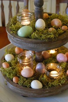 two tiered trays filled with eggs and candles on top of a table covered in moss