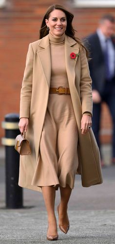 a woman walking down the street wearing a tan coat and dress with a rose on it