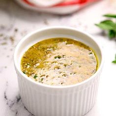 a small white bowl filled with soup on top of a marble counter next to green leaves