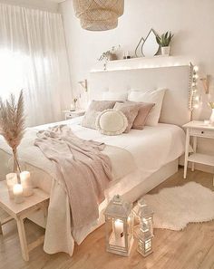 a white bed sitting in a bedroom next to two tables with candles on it and a basket hanging from the ceiling