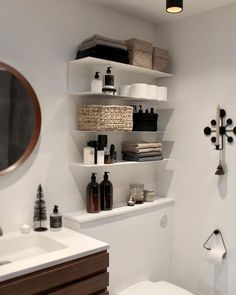 a white toilet sitting under a bathroom mirror next to a shelf filled with bottles and soaps