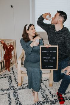 a man and woman sitting on a chair drinking from bottles in their hands, with a baby crib behind them