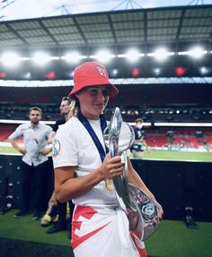 a woman holding a trophy and wearing a red hat in front of a stadium filled with people