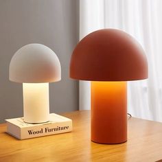 two lamps sitting on top of a wooden table next to a book and lamp shade