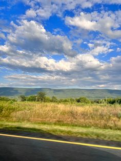 the view from a moving car on a road with mountains and clouds in the background