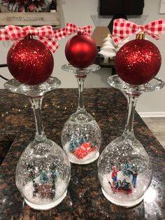 three wine glasses with christmas ornaments in them sitting on a counter top next to a red ornament