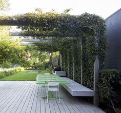 an outdoor dining area with green tables and white chairs, surrounded by greenery on either side