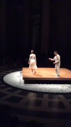 two people standing on top of a wooden platform in the middle of a dark room