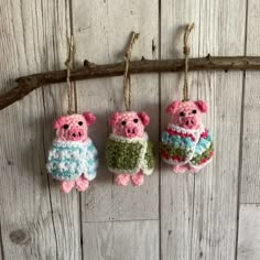 three crocheted pig ornaments hanging from a branch on a wooden wall with wood planks