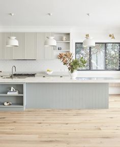 a large kitchen with white cabinets and wood flooring is pictured in this image, there are two lights hanging above the island