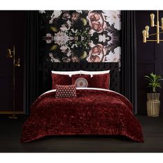 a bed with red comforter and pillows in front of a floral wallpapered room