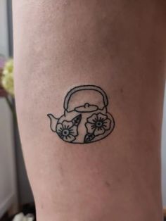 a small tattoo on the leg of a woman's thigh shows a teapot with flowers in it