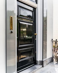 a black door on the side of a white building with gold trim and glass panes