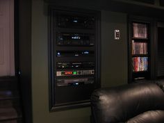 a living room with black leather couches and dvd's on the wall in front of bookshelves