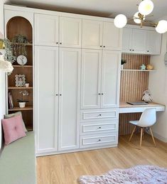 a bedroom with white cabinets and pink pillows on the floor next to a desk in front of a window